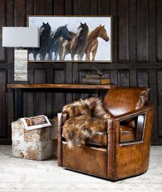 a brown chair sitting in front of a wooden table next to a painting on the wall