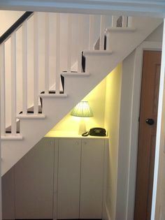 a lamp is on under the stairs next to a white cabinet and cupboard with drawers