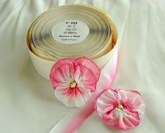 two rolls of ribbon with pink flowers on white cloths next to one roll of tape