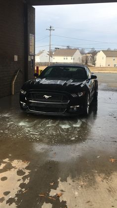 a black car parked in front of a building on a wet street with puddles of water