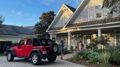 a red jeep parked in front of a house with two people standing outside the house