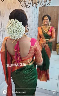 a woman in a green and orange sari with flowers on her head looking into the mirror