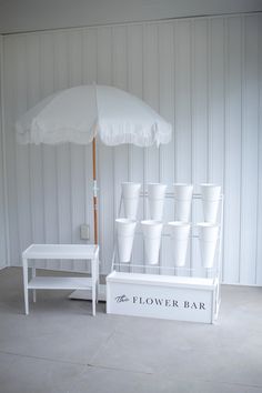 there is a white table with cups on it and an umbrella