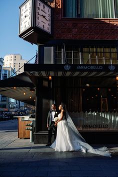 a bride and groom standing in front of a clock on the side of a building