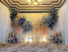 two white chairs sitting in front of a stage decorated with flowers