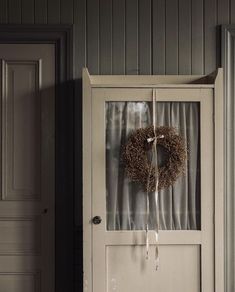 an old door with a wreath hanging on it's side and curtains behind it