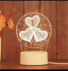 an illuminated lamp with two hearts and the word i love you on it in front of a vase filled with flowers