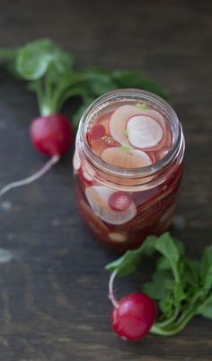 a jar filled with liquid sitting on top of a table next to radishes