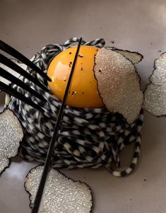 an orange sitting in a black and white basket with forks sticking out of it's sides