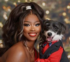 a woman holding a dog in her arms and posing for the camera with christmas lights behind her