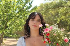 a woman holding flowers in her hand and looking at the camera