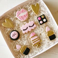 decorated cookies in a white box with pink and gold decorations on it, including eyelashes, lipstick, eye shadow, lips, lashes