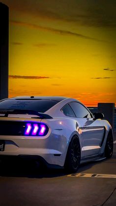 a white car parked in front of a tall building at night with the sun setting behind it