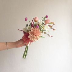 a hand holding a bouquet of flowers on a white wall with no one around it