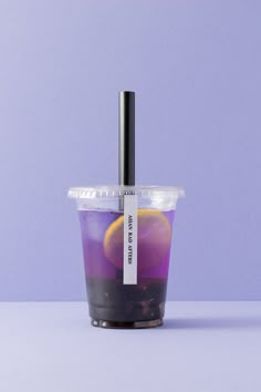 a plastic cup filled with purple liquid and an orange slice on the top, sitting on a table