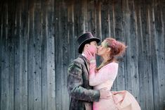 a man and woman are kissing in front of a wooden fence with pink paint on their faces