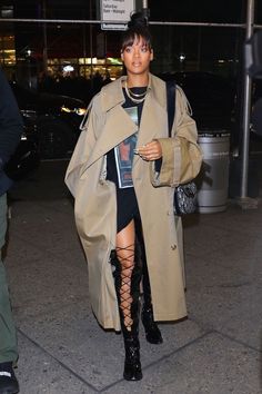 a woman in a trench coat and thigh high boots is seen walking down the street