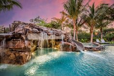 an outdoor pool with waterfall and slide surrounded by palm trees at sunset or sunrise time