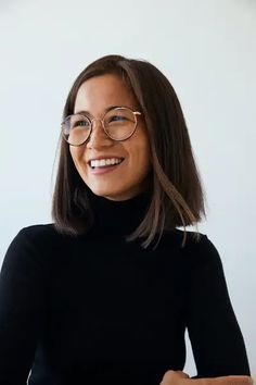 a woman wearing glasses and smiling at the camera with her hands on her hips while sitting in front of a white wall