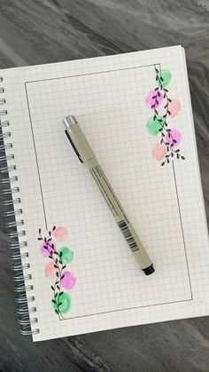 a pen sitting on top of a notepad with watercolor flowers and leaves painted on it