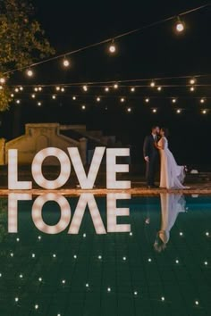 a bride and groom standing in front of the words love to me at night time