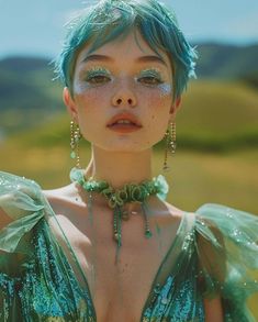 a woman with green hair and blue eyes is posing for a photo in front of mountains