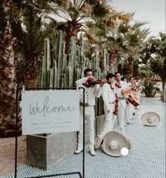 a group of men standing next to each other in front of a welcome sign and cacti