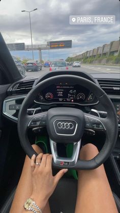 a woman driving an audi car on the road with her hands on the steering wheel