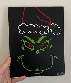 a hand holding up a black and green christmas card with the grin face drawn on it