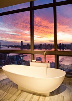 a bathtub sitting in front of a window overlooking a cityscape at sunset