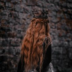 a woman with long red hair wearing a crown on her head, standing in front of a stone wall