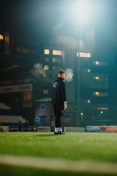 a man standing on top of a lush green field next to a soccer field at night