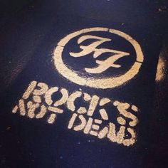 the words rock's not dead written in white chalk on a black surface with yellow paint