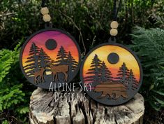 two necklaces with trees and mountains on them are hanging from a tree stump in the woods