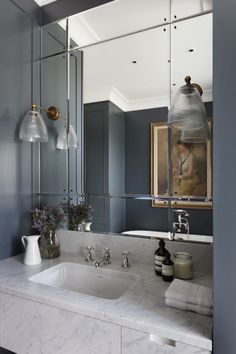 a bathroom with blue walls and marble counter tops, two lights on either side of the sink