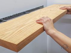 a person is holding the edge of a wooden shelf