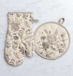 two oven mitts and a pot holder on a marble countertop with floral designs