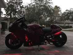 a red motorcycle parked on top of a brick road next to a tree filled street