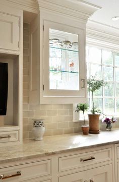 a kitchen with white cabinetry and marble counter tops, potted plants on the window sill