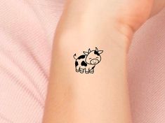 a small black and white cow tattoo on the left inner arm, with a pink shirt behind it