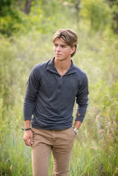 a young man standing in tall grass with his hands in his pockets