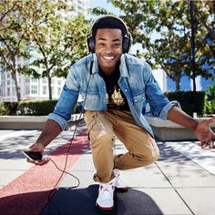 a smiling man with headphones on sitting on a skateboard and listening to music