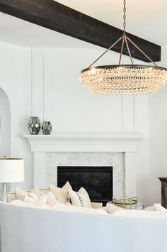 a chandelier hangs from the ceiling above a fireplace in a white living room