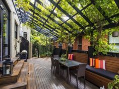 a wooden deck with benches and tables under a pergolated roof