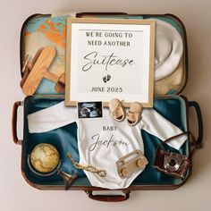 an open suitcase filled with baby items and a sign that says we're going to need another