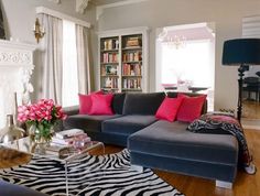 a living room filled with furniture and a fire place covered in pink pillows on top of a hard wood floor