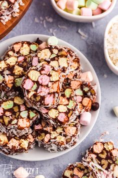 a white plate topped with chocolate covered marshmallows next to bowls of candy