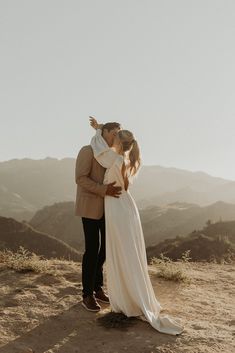 a bride and groom kissing on top of a mountain