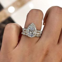 a woman's hand with two wedding rings on top of her finger and the ring has an oval shaped diamond