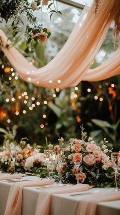 Elegant wedding reception in a garden with soft peach and ivory draping, adorned with lush greenery and cascading floral centerpieces. Ambient fairy lights create a romantic glow. Photographed in natural light.